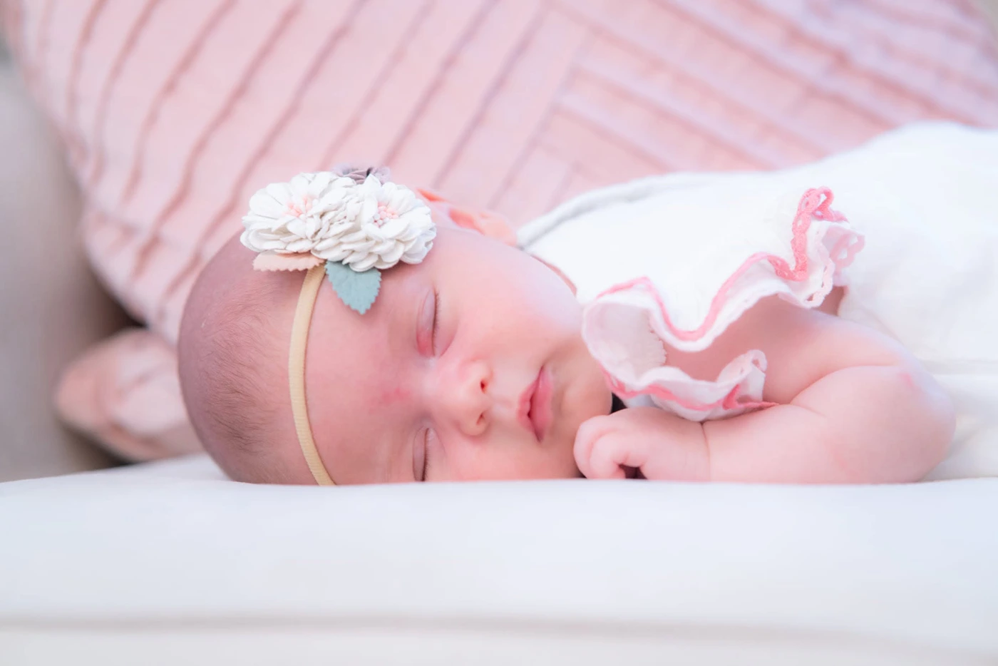 Sleeping newborn wearing a floral headband on a soft pink backdrop